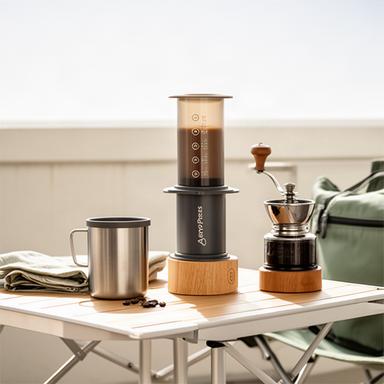 AeroPress mit Kaffeebecher und Handmühle auf einem hellen Reisetisch